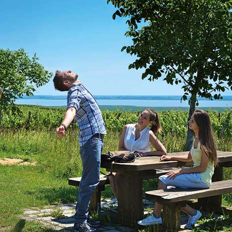 Pause vom Wandern, Mann streckt sich, zwei Damen sitzen auf einer Bank